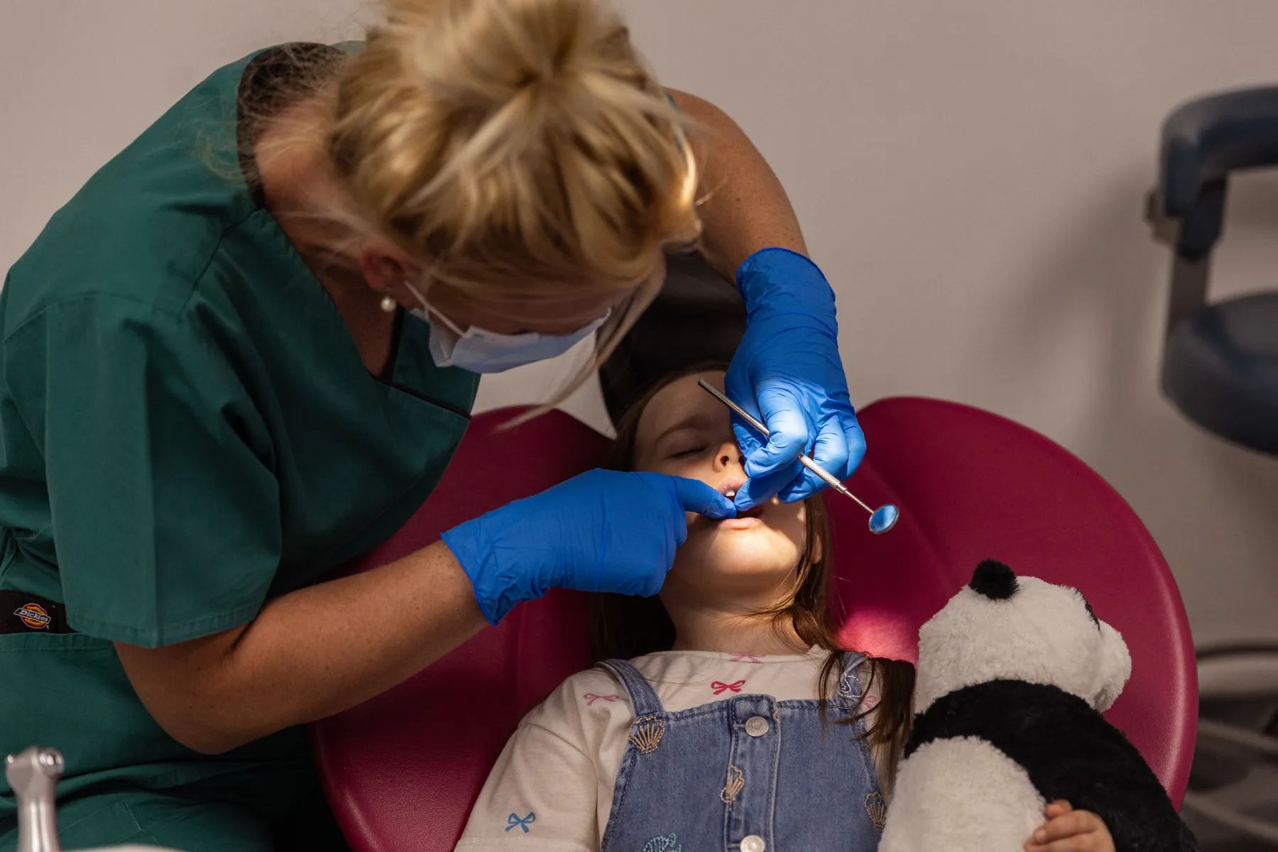 Dental nurse checking a young patient's teeth, panda toy beside her